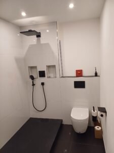 Komplettsanierung eines Bades in Heidelberg - Verlegung von Großformat-Wandfliesen in Weiß - zwei Ablagen in der Dusche